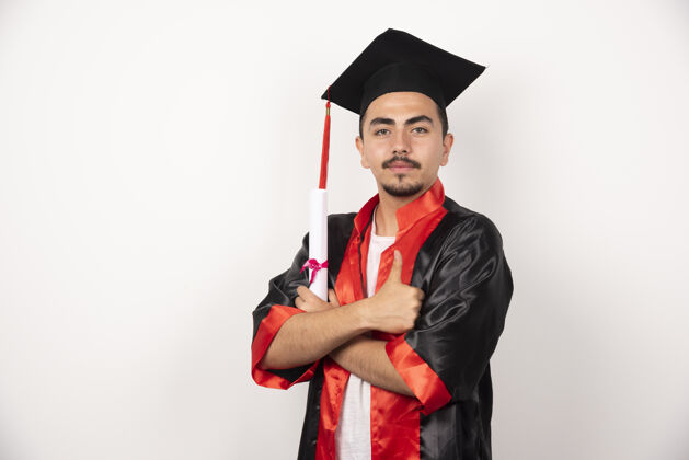 举行年轻的男生拿着毕业证书在白色衣服上摆姿势证书长袍成就