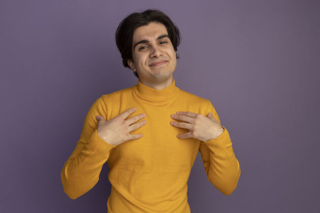 帅哥高兴的年轻帅哥穿着黄色高领毛衣把自己的手孤立在紫色的墙上高领毛衣年轻手
