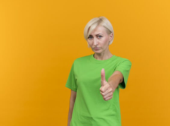 感情自信的中年金发斯拉夫女人在看前面展示大拇指孤立在黄色的墙壁与复制空间表演拇指公民