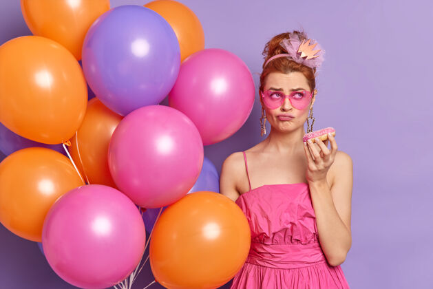 裙子郁闷不满的美女在节日聚会上感到无聊等待许久开始捧着甜甜圈和一串五彩气球太阳镜站着派对