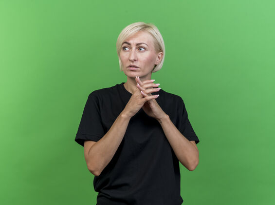人体贴的中年金发斯拉夫女人双手合十 看着隔离在绿色墙壁上的一面 还有复制空间人金发衣服