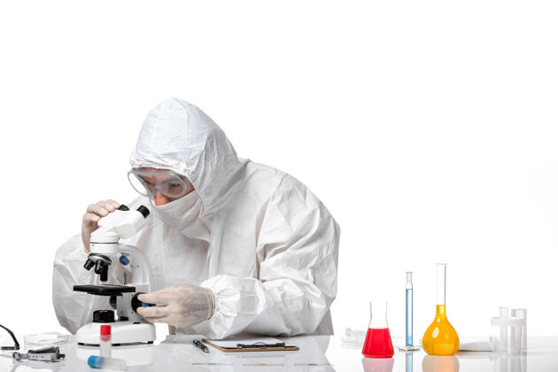 健康正面图：男医生穿着防护服 戴着口罩 在白色办公桌上使用显微镜病毒人人