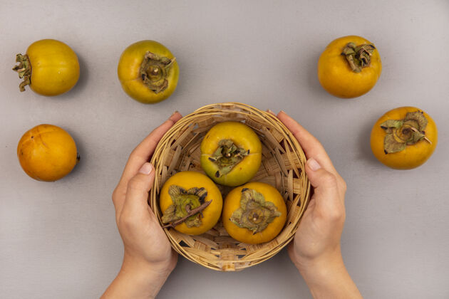 橘子顶视图女性双手捧着一桶柿子果与柿子果隔离新鲜手顶部