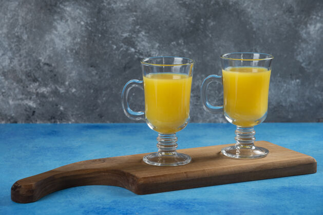 柑橘木板上放两杯鲜橙汁美味杯子水果