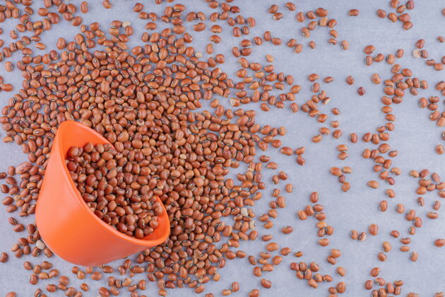 豆类在大理石表面的一堆红豆里放着一个橙色的小碗豆美味配料
