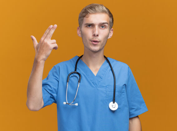 制服自信的年轻男医生穿着医生制服 手持听诊器 在橙色的墙上显示出的姿势展示手势医生