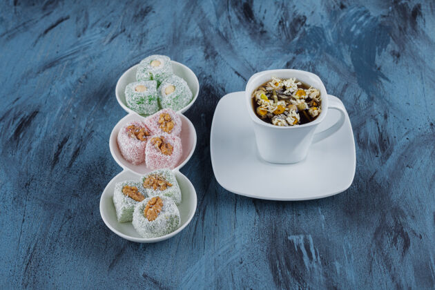 茶白色的碗里放着各种甜食 蓝色的表面放着坚果和茶玫瑰鲜花枇杷