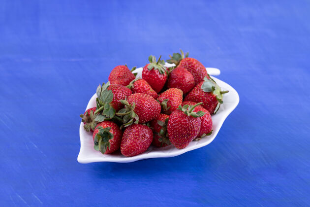 丰满在蓝色的表面上放满草莓的白色盘子营养可口草莓