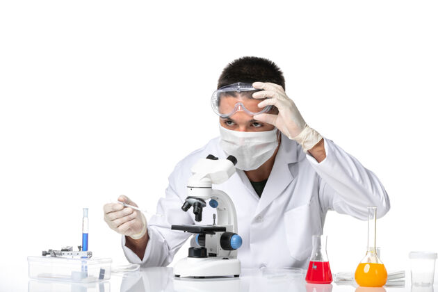 实验室外套前视图：男医生穿着白色医疗服 戴着面罩 在白色空间使用显微镜专业显微镜病毒