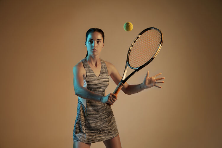 射击一位白人女子在混合霓虹灯下孤立地打网球 背景是棕色适合年轻女性运动员在运动比赛中运动或动作运动 运动 健活方式的概念明亮运动年轻人