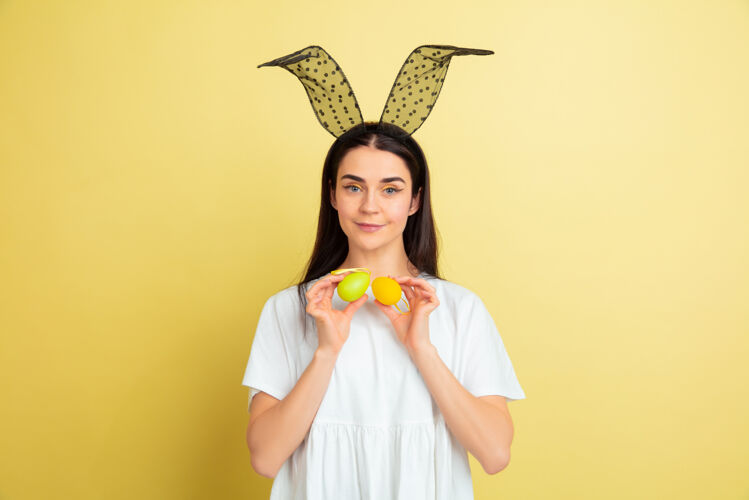 鸡蛋寻找彩蛋来了白人妇女作为一个复活节兔子在黄色的工作室背景复活节快乐的问候美丽的女模特人类情感的概念 面部表情 节日复制空间人类漫画兔子