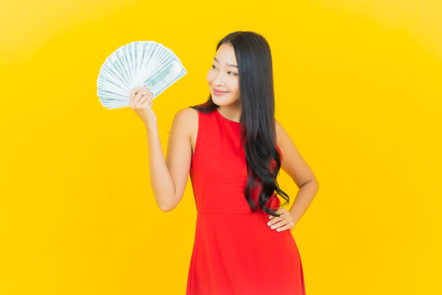 账单画像美丽的亚洲年轻女子微笑着在黄色的墙上有很多现金和金钱女士欢乐女性