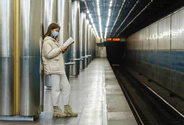 外科口罩在地铁站看书的年轻女子公共服务地铁站防护