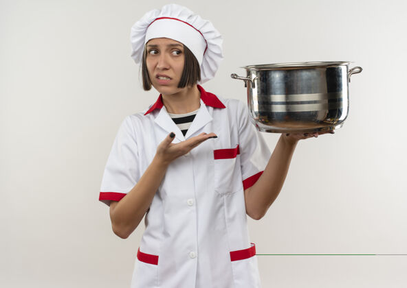 壁板穿着厨师制服的年轻女厨师手拿着并指着锅 看着在白色背景上有复制空间的隔离边指着烹饪不愉快