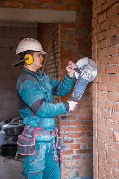 建筑一个戴着安全帽的电工建筑工人在一个工作场所用研磨机工作专业人员锯切割承包商