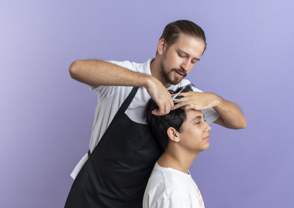 帅哥年轻帅气的理发师穿着制服在紫色背景上为年轻客户理发穿理发师理发