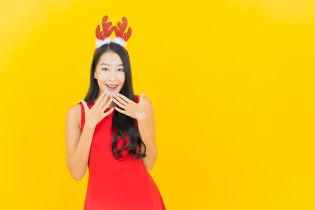 年轻肖像美丽的亚洲年轻女子戴圣诞帽或发带在黄色的墙上欢呼礼物快乐