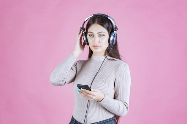 服装戴着耳机在智能手机前放音乐的女孩女人人类女性