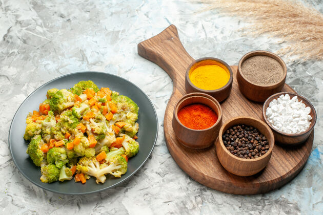 烹饪健康蔬菜沙拉的侧视图不同的香料放在白色桌子的砧板上膳食壁板切