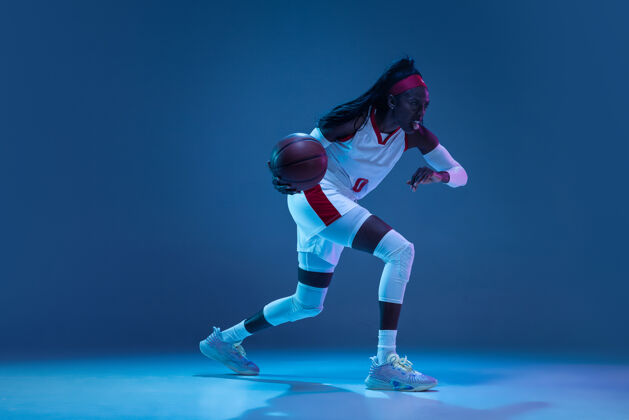 运动员美丽的非洲裔美国女篮球运动员在运动和行动中 在霓虹灯的蓝色墙壁上健活方式的概念职业体育爱好团队比赛赢家