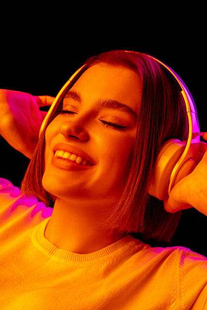 专业音乐流行霓虹灯下粉红色工作室背景上的白种女人肖像戴着耳机的漂亮女模特人类情感的概念 面部表情 销售 广告 时尚明亮音乐家耳机