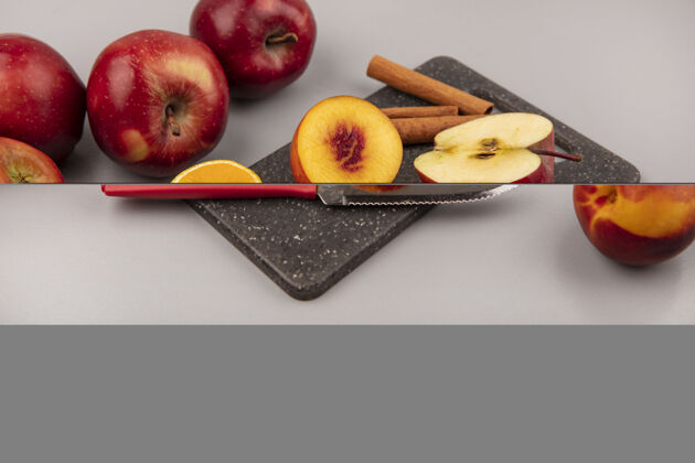 新鲜黑色厨房板上美味的半个桃子的俯视图 灰色背景上有橘子苹果和肉桂棒 刀子放在上面苹果饮食美味