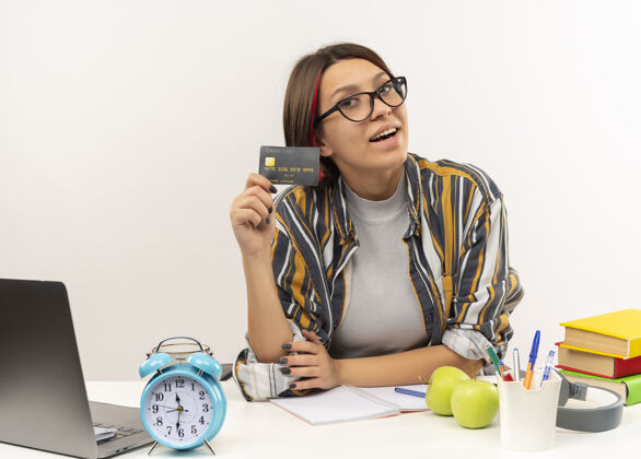 学生快乐的年轻学生女孩戴着眼镜坐在办公桌上显示信用卡隔离在白色眼镜信用年轻
