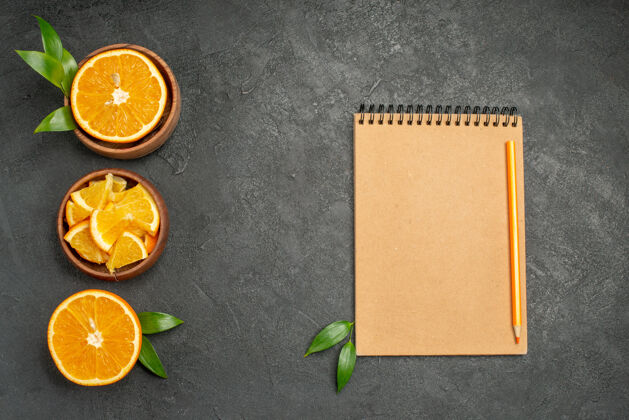块一套切成两半片的新鲜橘树叶和笔记本放在黑桌子上半空切片