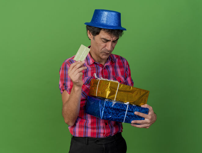 绿色一个中年白种人 戴着派对帽 拿着礼包和信用卡 看着隔离在绿色背景上的礼包 还有复印空间礼物聚会帽子