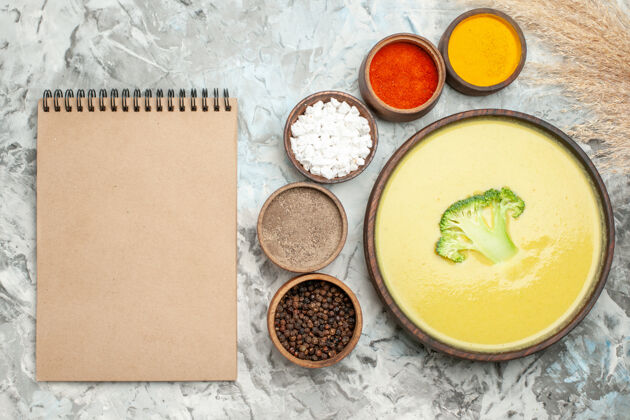餐厅奶油西兰花汤在一个棕色的碗和不同的香料旁边的笔记本在灰色的桌子上不同晚餐碗