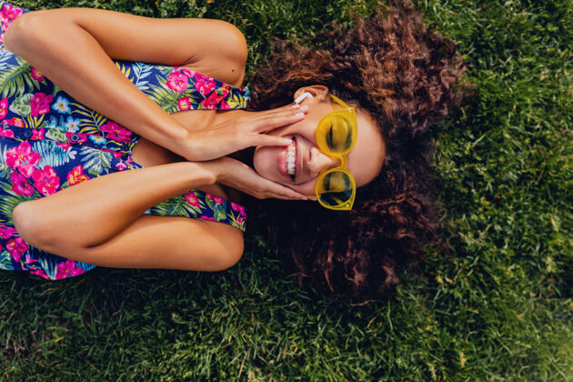 黄色年轻时尚的黑人女子 戴着无线耳机听音乐 躺在公园的草地上玩得很开心 夏日的时尚风格 五颜六色的时髦装扮 俯瞰风景非洲裔美国人情绪享受