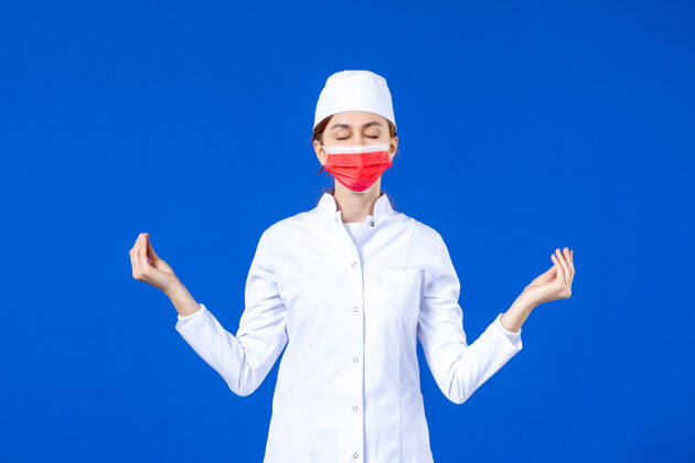 防护正面图身着医疗服的年轻护士 蓝色墙上戴着红色防护面具专业医学人