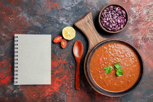 一餐番茄汤豆和笔记本的水平视图在一个混合颜色的桌子上的砧板上黑板胡椒粉豆类