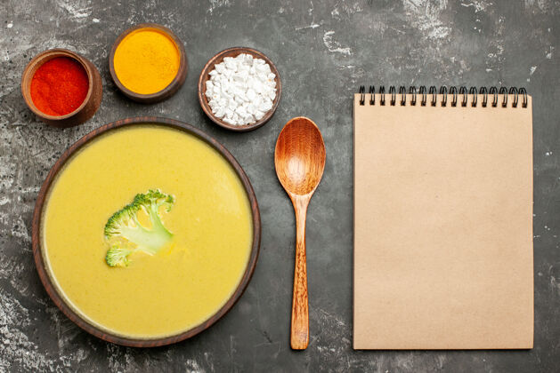 炊具奶油西兰花汤在一个棕色的碗不同的香料汤匙和笔记本在灰色的桌子上抹刀餐具餐厅