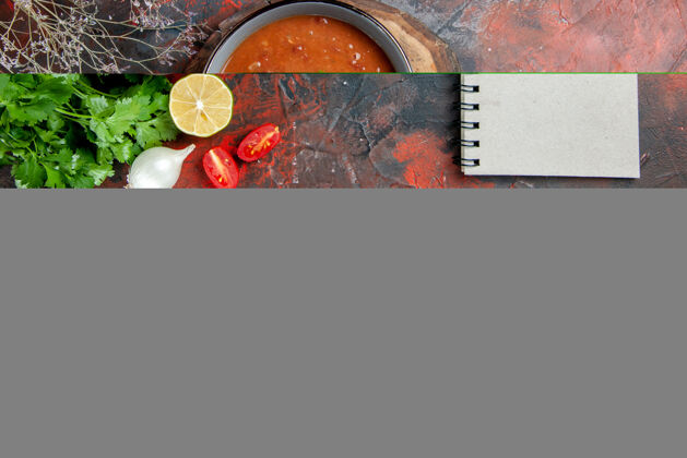 新鲜的上图：蓝色碗里的番茄汤放在木制托盘上 调羹豆 油瓶 大蒜和笔记本放在五颜六色的桌子上茶锅杯子