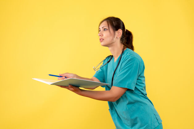 持有前视图穿着医用衬衫的女医生拿着黄色背景的笔记健康成人肖像