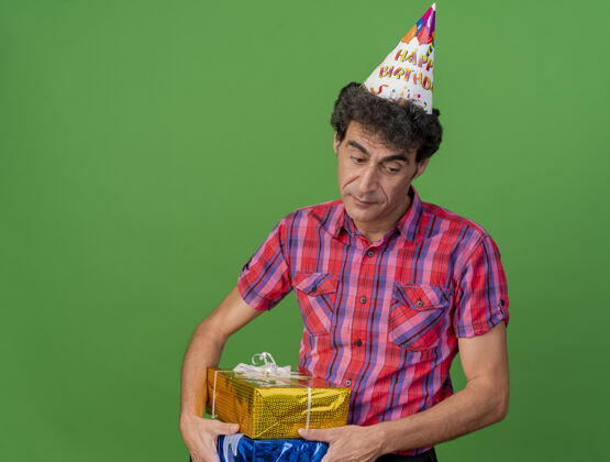 帽子悲伤的中年白种人聚会男子戴着生日帽拿着礼包在绿色背景上看着孤立的复制空间空间举行礼物