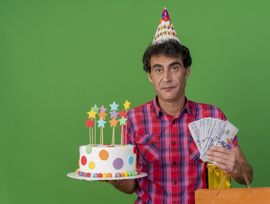 礼物中年白种人聚会男子戴着生日帽拿着生日蛋糕纸袋礼包和钱看着隔离在绿色背景上的相机和复印空间持有钱包