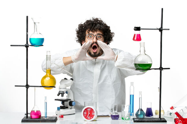 周围正面图身着特殊套装的年轻男性科学家站在桌子旁 拿着解决方案呼吁白墙科学实验室的化学大流行实验室外套外套实验室