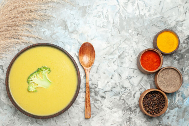 碗棕色碗中的奶油西兰花汤和灰色桌子上的不同香料的水平视图勺子容器调味品