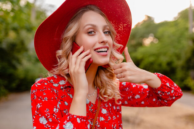 明亮迷人的时尚金发微笑的妇女在稻草红色帽子和衬衫夏季时尚服装画像在电话交谈积极的姿态情感脸情感年轻