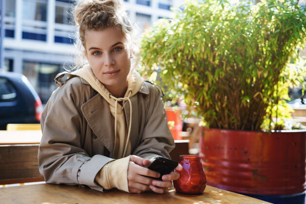等待年轻的女咖啡馆客户坐在户外 用手机咖啡桌子设备