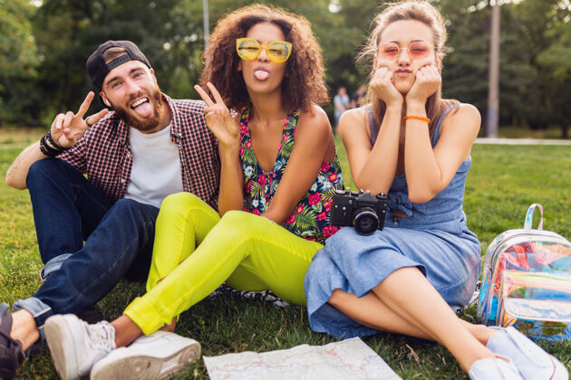 朋友快乐的年轻朋友们一起坐在公园里 男女同乐 带着相机旅行 搞笑动情多种族酷太阳镜