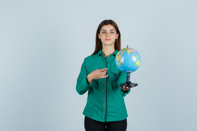 前面穿着衬衫的年轻女士拿着地球仪 指着地球仪 看上去很自信 正对着地球仪眼睛头发黑发