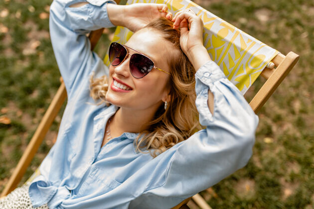 手提包迷人的金发微笑的女人坐在躺椅上穿着夏天的衣服快乐漂亮放松
