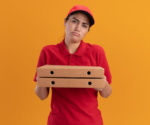 戴着悲伤的年轻送货女孩穿着制服 戴着帽子 手里拿着披萨盒 被隔离在橙色的墙上悲伤制服女孩