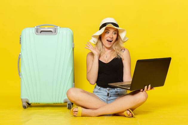 视野前视图年轻女性使用笔记本电脑在黄墙上航行度假女性旅行旅行太阳成人漂亮微笑