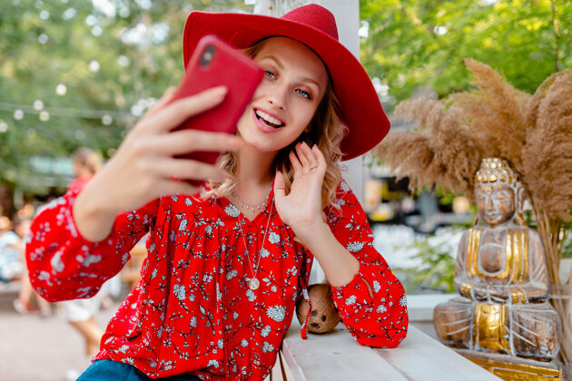 情感迷人的时尚金发微笑的女人在稻草红色帽子和衬衫夏季时尚服装拍照自拍智能手机咖啡厅金发脸姿势
