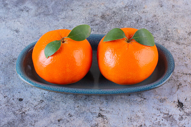 有机两个新鲜的橘子在灰色盘子上的特写照片切割柑橘变异