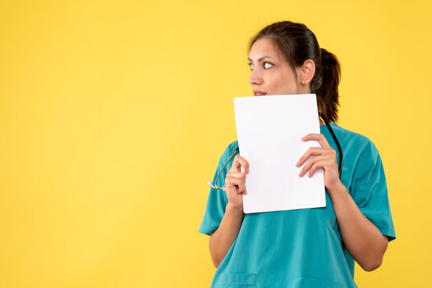 人正面图黄色背景下穿着医疗衫的女医生拿着纸分析健康病毒持有
